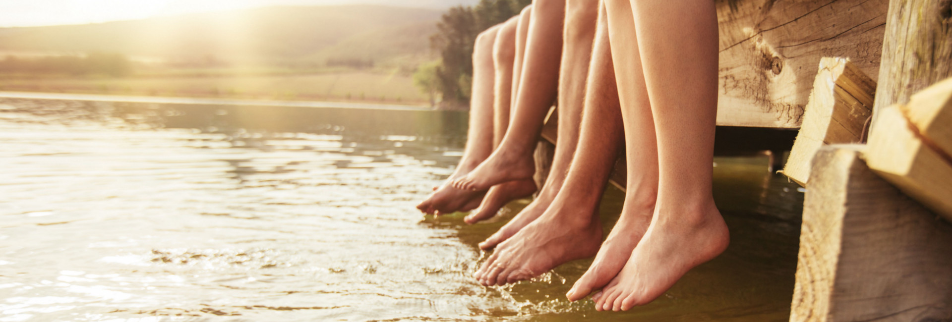 Mehrere Menschen sitzen auf einem Steg und lassen die Füsse über dem Wasser baumeln